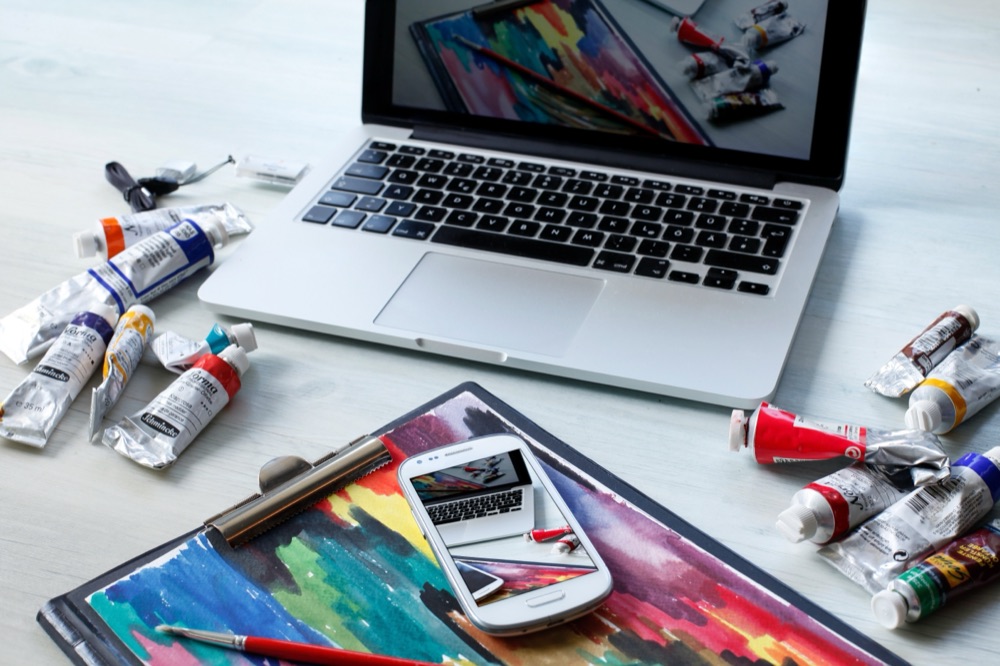 A creative workspace with artwork displayed on a laptop and phone