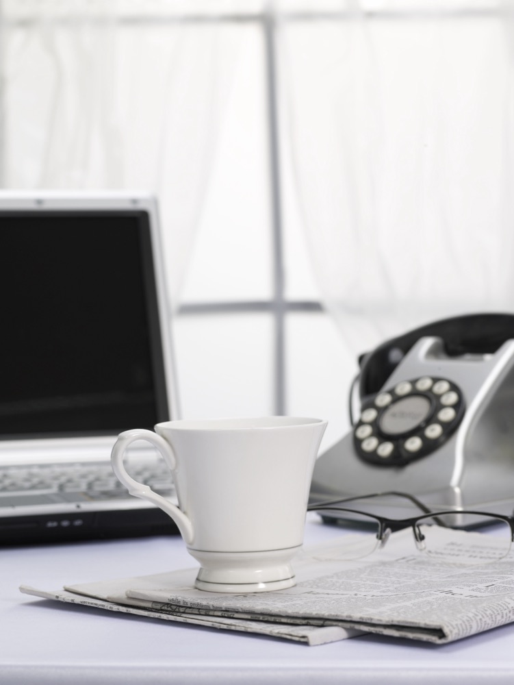 A telephone, laptop and coffee on a desk